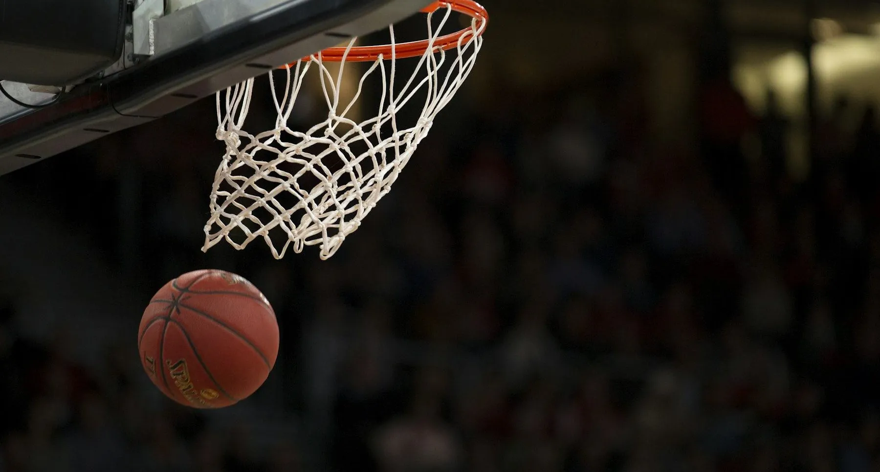 Basketball dropping through the net in an arena, crowd lights blurred behind