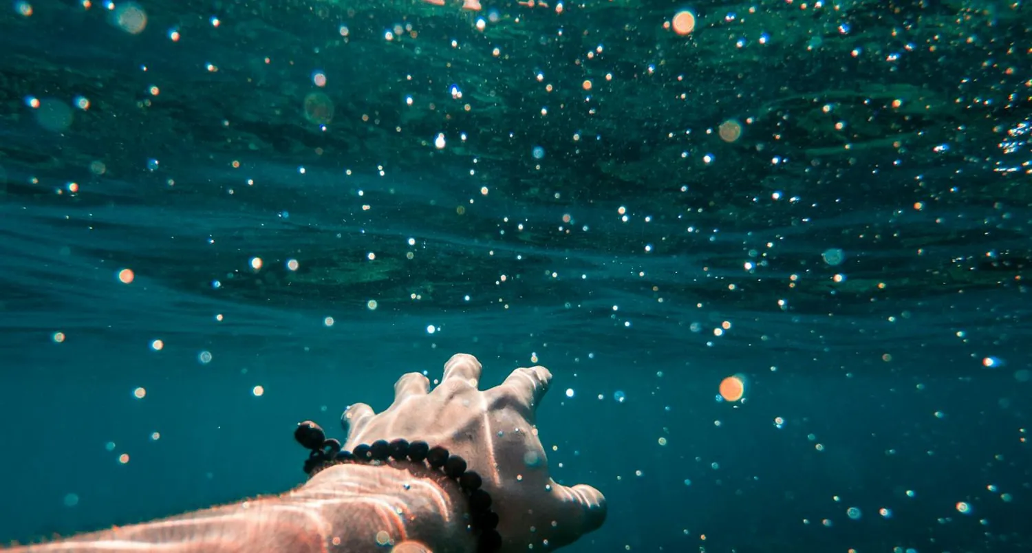 Underwater: a swimmer's hand and bubbles breaking toward the surface in deep teal water
